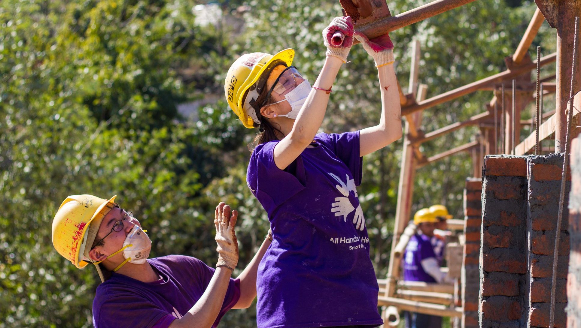 All Hands and Hearts volunteers in construction gear, cleaning wood.