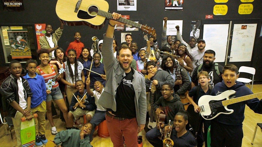 Chad Bernstein holding guitar with Guitars Over Guns students