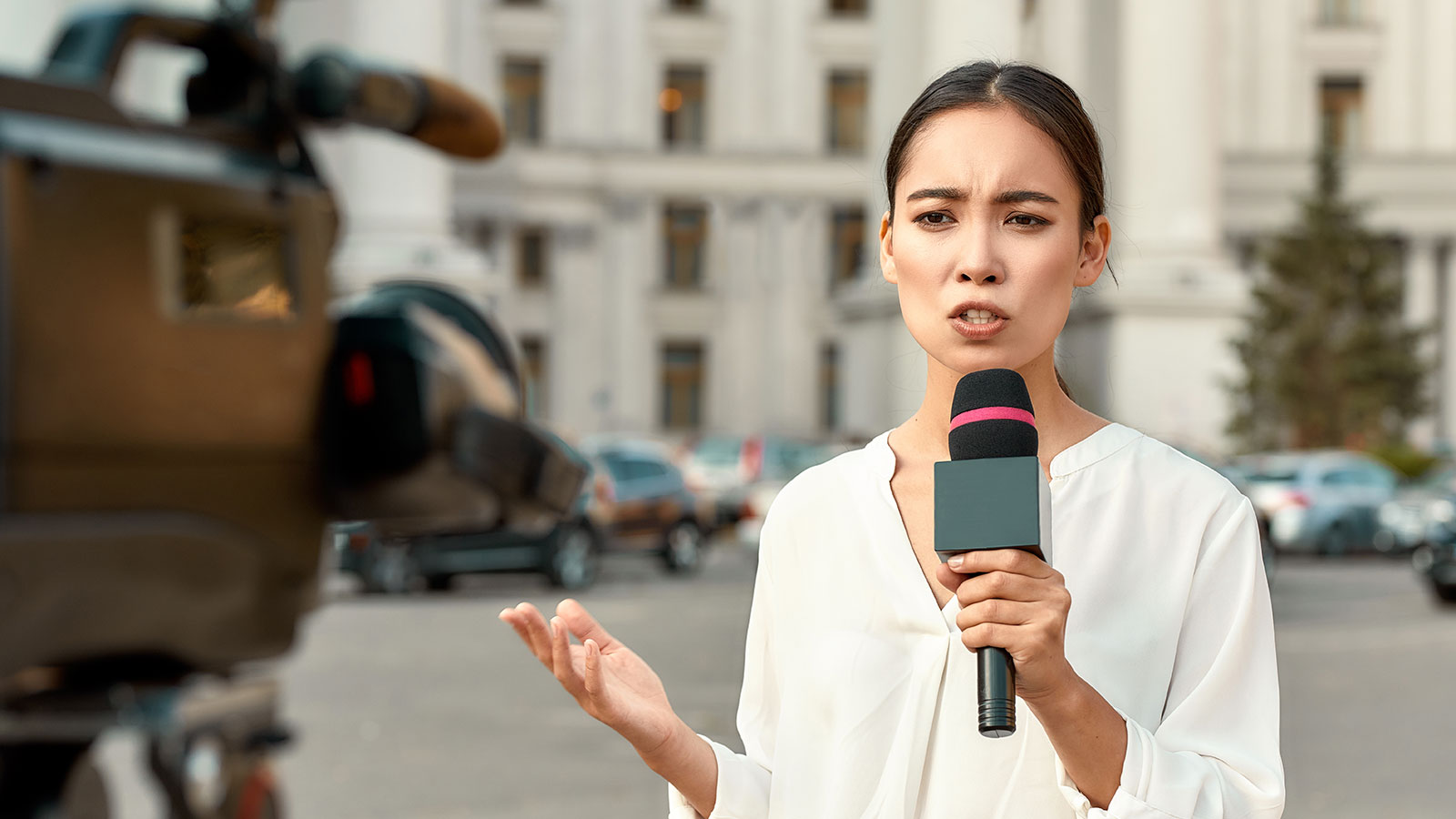Woman standing with a microphone in front of a news camera | NewsMatch Woman standing with a microphone in front of a news camera | NewsMatch