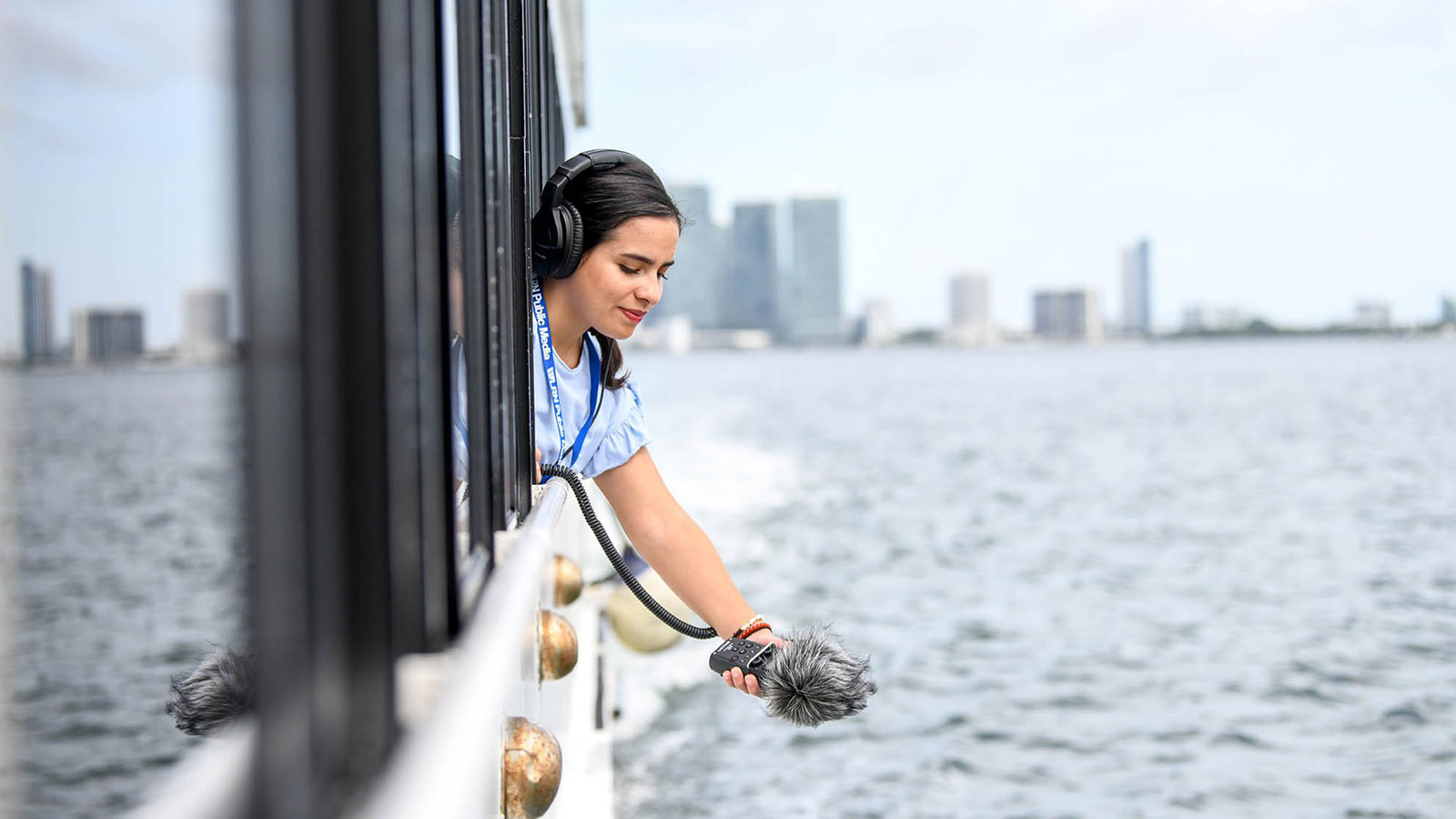 Woman with microphone leaning out window on a boat | The Miami Foundation