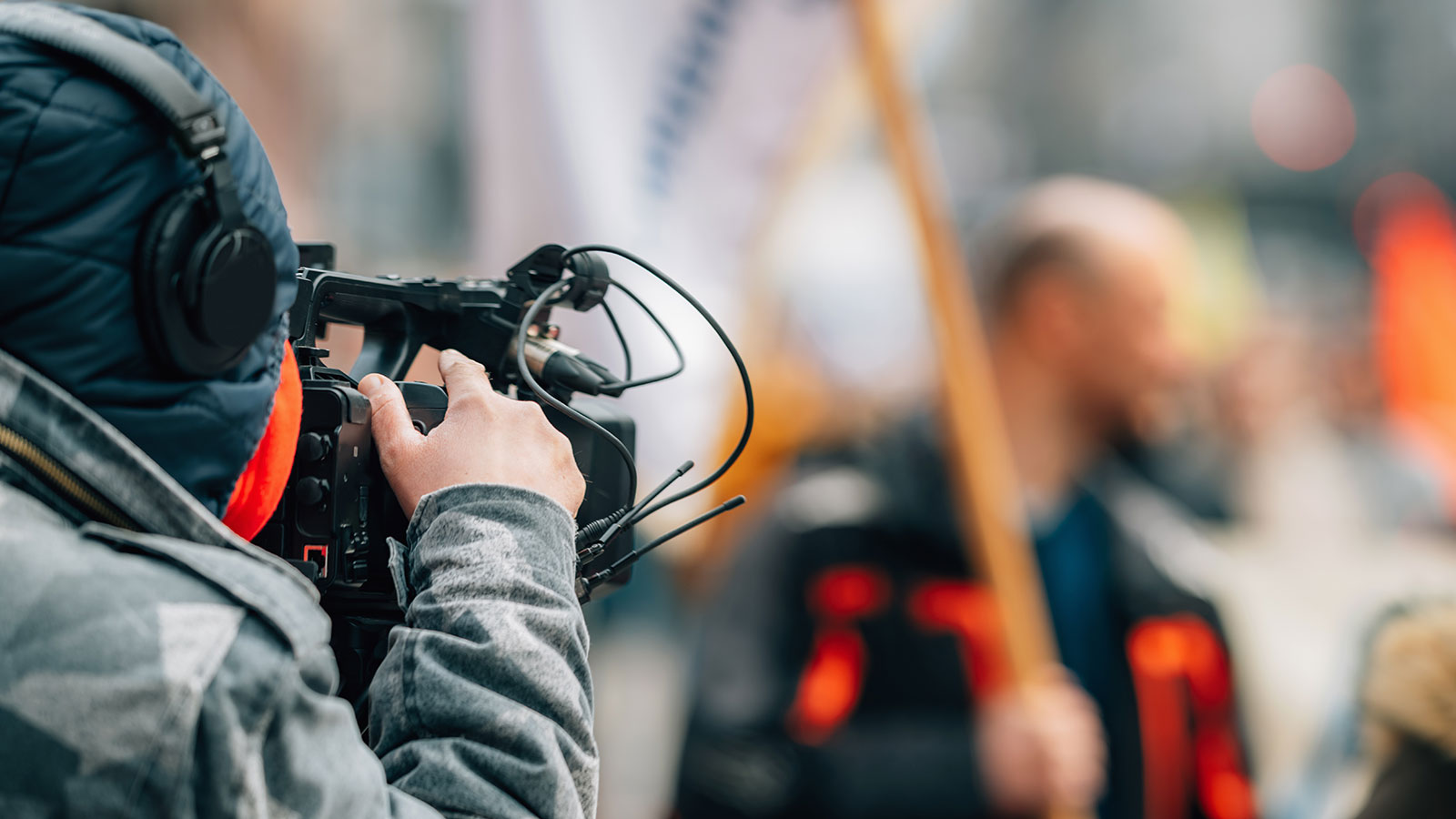 Person holding a camera looking at a man holding a flag | Sustainable Publishing Solutions Person holding a camera looking at a man holding a flag | Sustainable Publishing Solutions