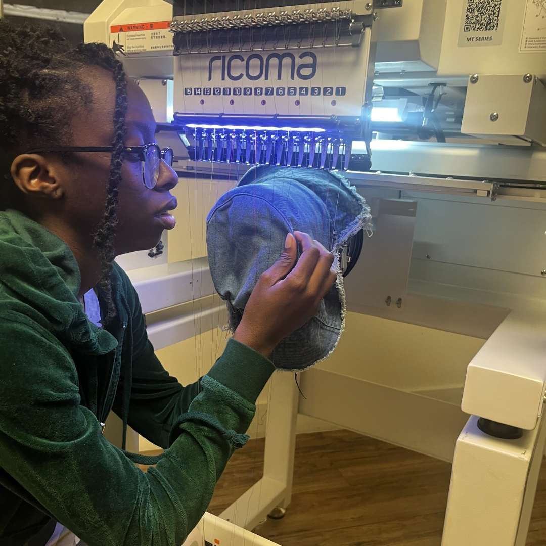 Woman works on embroidering a hat with a large embroidery machine purchased via Miami Open for Business.