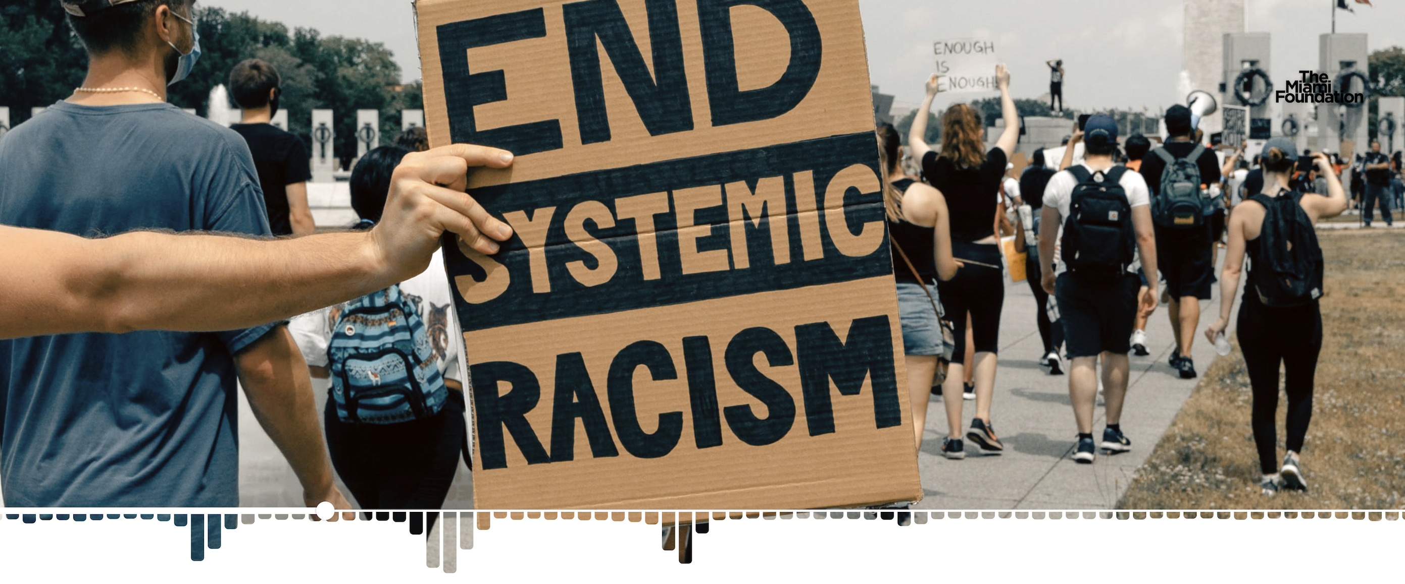 Protest march with hand holding sign saying "End systemic Racism" with The Miami Foundation logo in upper right corner Protest march with hand holding sign saying "End systemic Racism" with The Miami Foundation logo in upper right corner